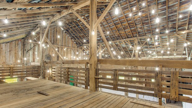 A spacious barn interior with wooden beams, a high ceiling, and multiple hanging lights. - Historic Barn/Lodge and 3 More - 2 Mi From Town (Rushville)