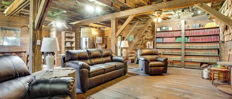 A rustic interior with wooden beams, leather sofas, a bookshelf, and a ladder.