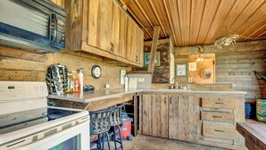A rustic kitchen with wooden cabinets, a stove, and a bar area. - Historic Barn/Lodge and 3 More - 2 Mi From Town (Rushville)