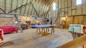 A loft bedroom with a sloped ceiling, wooden beams, a ping pong table, a bed, and a ladder. - Historic Barn/Lodge and 3 More - 2 Mi From Town (Rushville)
