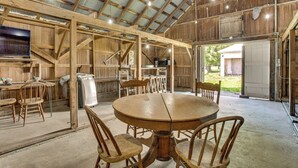 A rustic barn interior with a wooden dining table, chairs, and a large window. - Historic Barn/Lodge and 3 More - 2 Mi From Town (Rushville)
