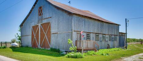 A large, rustic barn with a wooden door and windows, surrounded by a grassy area.