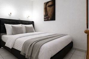 Ein Schlafzimmer mit einem Bett, Kissen, einer Decke, einer Wandleuchte und einem Gemälde.