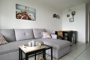 Ein modernes Wohnzimmer mit einem grauen Ecksofa, einem kleinen Tisch mit einer Kerze und einem Gemälde eines Segelbootes an der Wand.