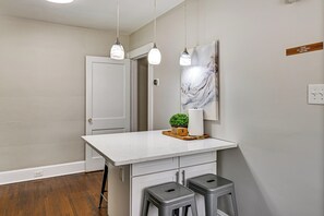 Eine Küche mit weißer Arbeitsplatte, zwei Barhocker, Pendelleuchten, einer Tür und einem an der Wand befestigten Schild.