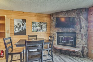 Ein Holzinterieur mit Kamin aus Stein, einem an der Wand befestigten Fernseher und einem Esstisch mit Stühlen.
