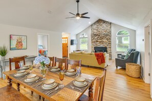 Un comedor con mesa de madera dispuesta para seis personas, una pared de acento de piedra, y una sala de estar con chimenea de piedra.