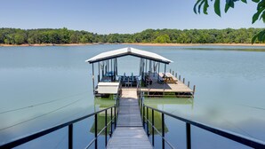 A wooden dock leading to a covered seating area with a view of a calm lake and forested shoreline. - Dock w/ Deep Water Levels! Home on Lake Hartwell (Anderson)