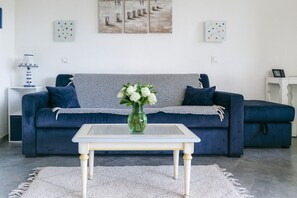 Ein Wohnzimmer mit einem blauen Sofa, einem weißen Couchtisch, einer Vase mit Blumen und Bildern an der Wand.