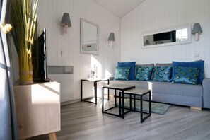 Ein Wohnzimmer mit grauem Sofa, zwei schwarzen Tischen, einem Spiegel und Wandlampen.
