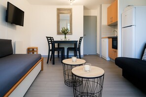 Ein kompakter Wohnbereich mit einer Couch, einem Esstisch mit Stühlen, einer kleinen Küchenzeile mit Kühlschrank und einem flachbildfernseher an der Wand.