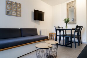 Ein modernes Wohnzimmer mit einer Couch, einem Fernseher, einem Esstisch mit Stühlen und einem kleinen Hocker.