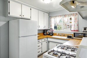 Una cocina con armarios blancos, estufa a gas, refrigerador y ventana con cortinas estampadas.