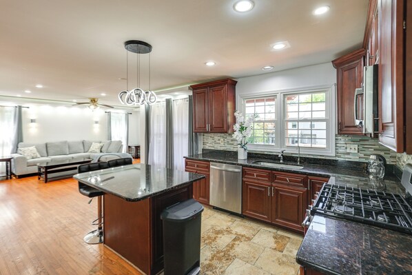 A modern kitchen with dark wood cabinets, a granite countertop, stainless steel appliances, and a dining area with a sofa and table. - 1 Mi to Main St! Family-Friendly Reisterstown Home (Reisterstown)