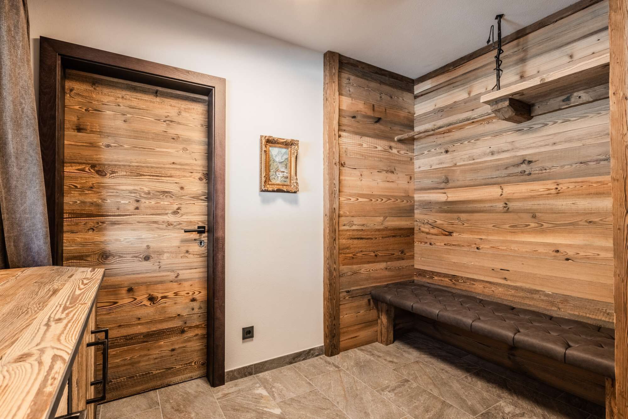 A wooden interior with a bench, a door, and a framed picture on the wall.