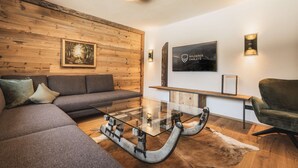 Un salon moderne avec un mur en bois, un canapé, une table basse en verre, un téléviseur fixé au mur et un luminaire fixé au plafond.