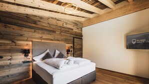 Une chambre moderne avec un plafond en bois, un lit recouvert de linge blanc, un luminaire fixé au mur et un tableau encadré.