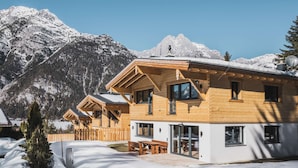 Un chalet en bois, avec un toit enneigé, de grandes fenêtres et une vue sur des montagnes aux sommets couverts de neige.