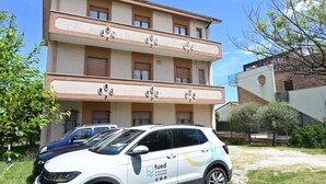 Ein mehrstöckiges Gebäude mit flacher Fassade und Balkonen, sowie ein weißer SUV mit einem Logo.