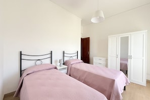 Un dormitorio con dos camas, un armario blanco y una mesita de noche con lámpara.