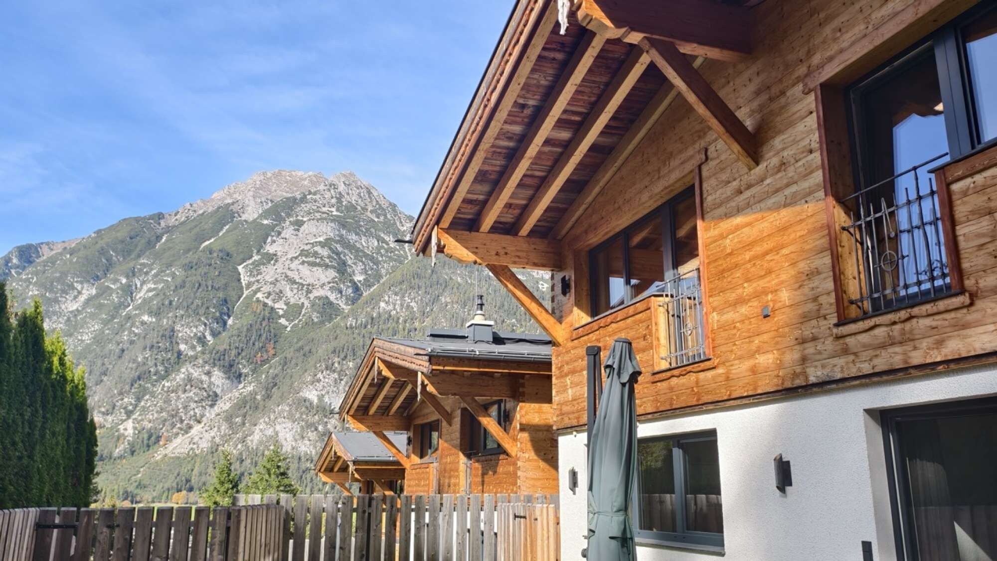 En træchalet med balkon foran et bjerglandskab.
