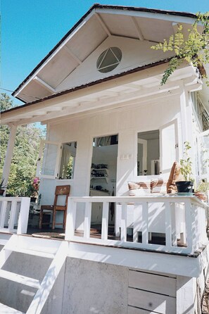 A white building with a covered porch, a circular window, and a door leading to an interior space. - Tiny Villa in Nature With Epic Sunrise View (Gili Trawangan)