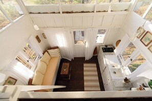 A compact, single-level room with a sofa, a small table, a sink, and a window providing a view of the outdoors. - Tiny Villa in Nature With Epic Sunrise View (Gili Trawangan)