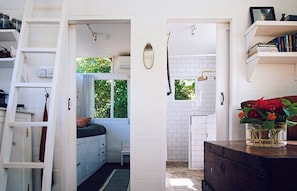 A compact kitchen with white cabinets, a window, and a small bathroom with a shower. - Tiny Villa in Nature With Epic Sunrise View (Gili Trawangan)