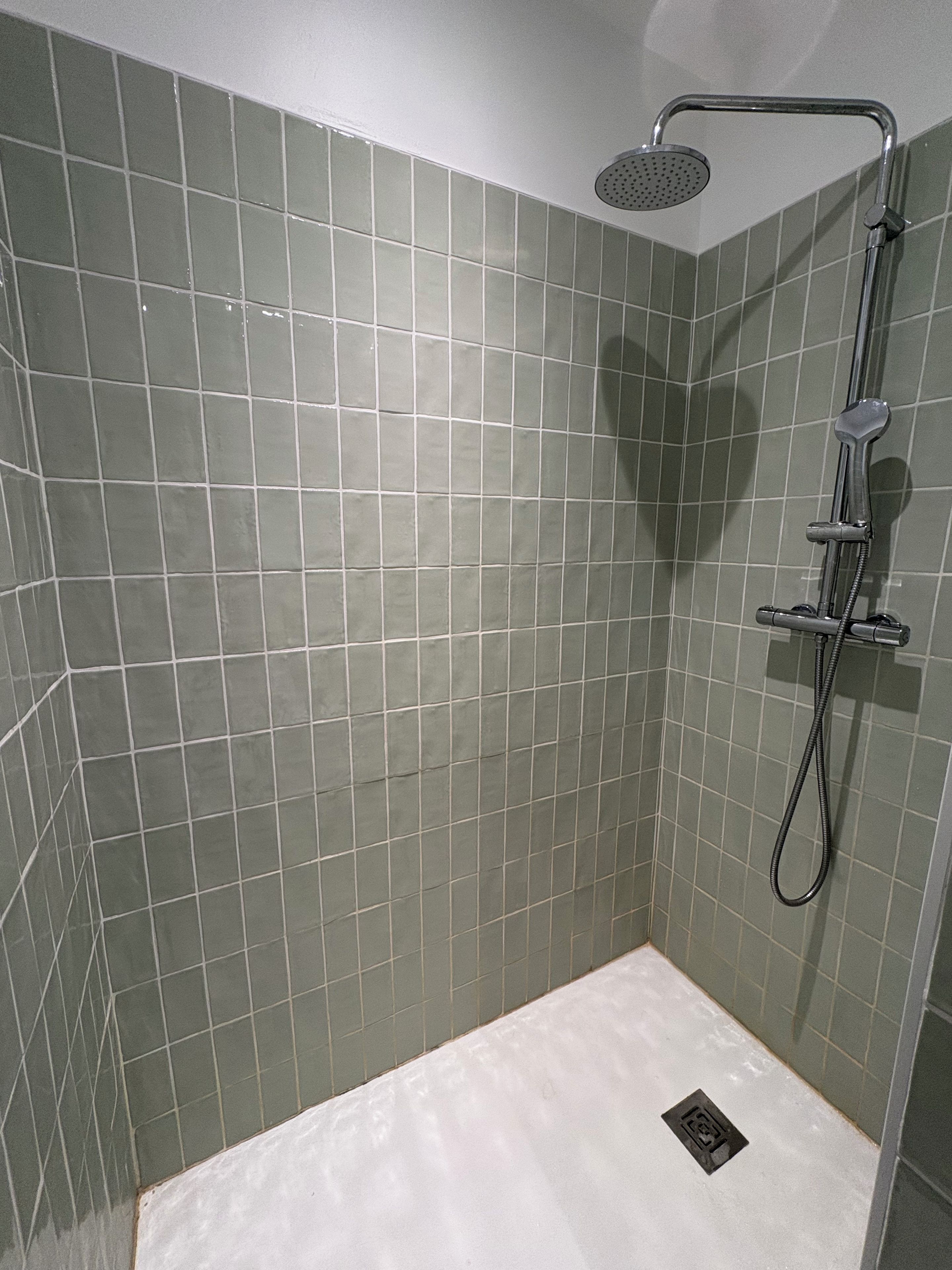 A shower area with a handheld showerhead and a wall-mounted faucet.