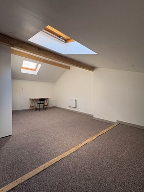 Um quarto com teto inclinado, um claraboia, uma mesa com cadeiras e um radiador.