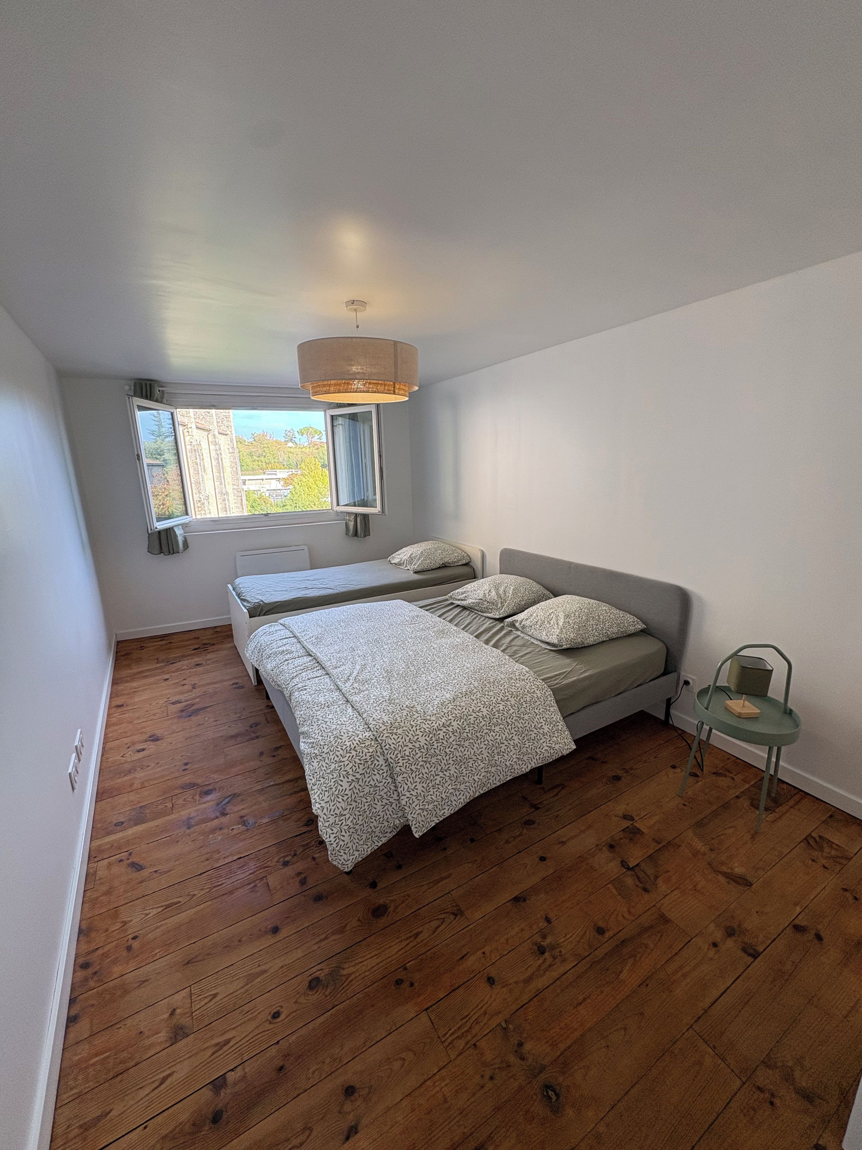 A bedroom with a bed, a window, a hanging light fixture, and a chair.