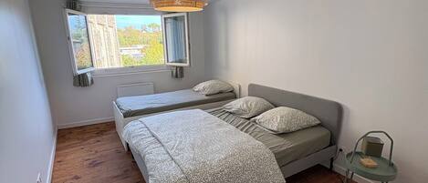 A bedroom with a bed, a window, a hanging light fixture, and a chair.