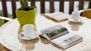 A round table with a potted plant, two cups with saucers, and an open book.