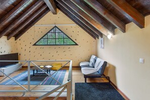 Ein Loft-Zimmer mit schrägem Dach, einem großen Fenster, einer Couch, einem Fernseher und einem Essbereich mit Tisch und Stühlen.