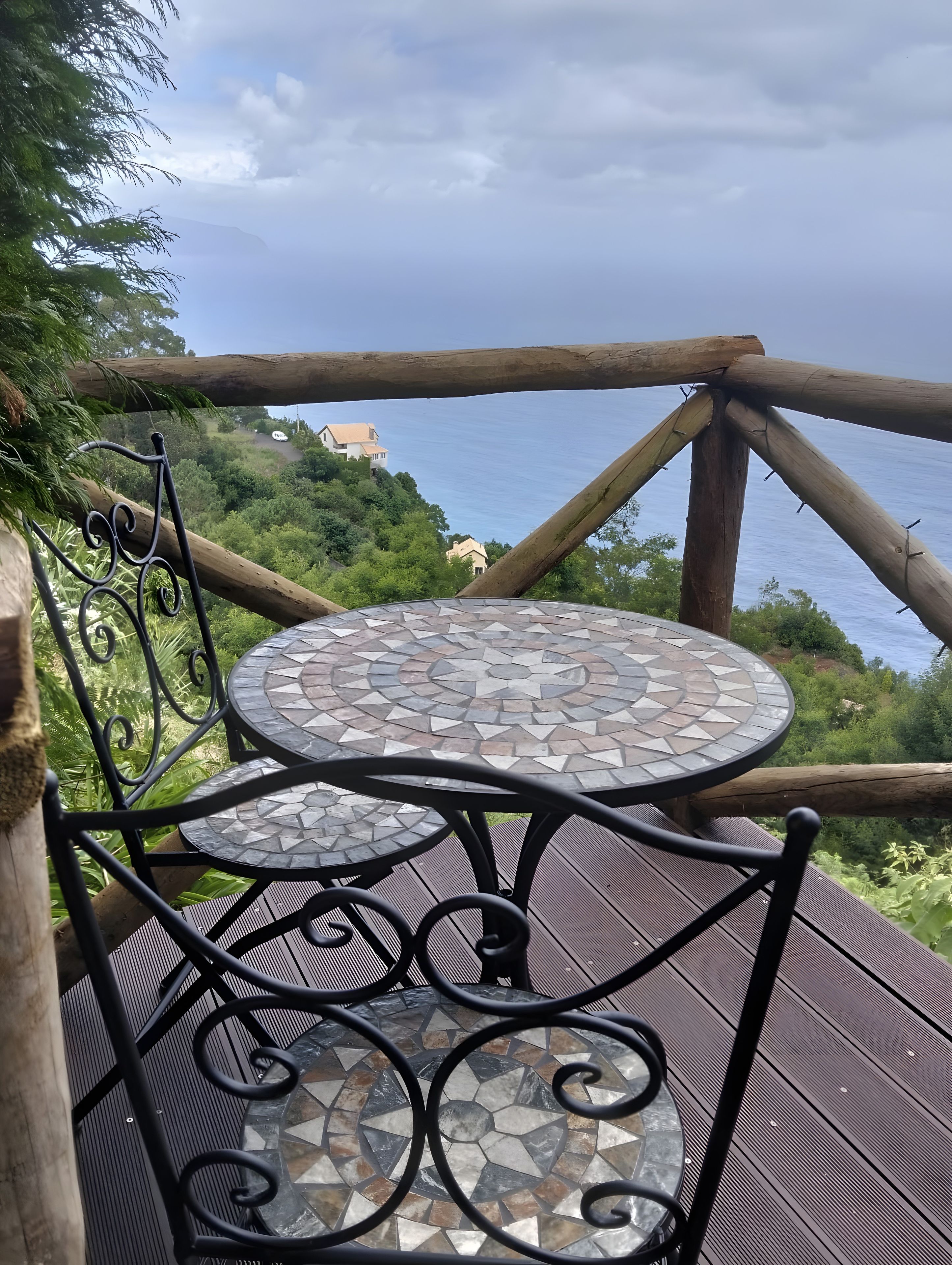 Une terrasse avec une table et des chaises décorées de mosaïques, offrant une vue sur un paysage côtier parsemé de maisons.