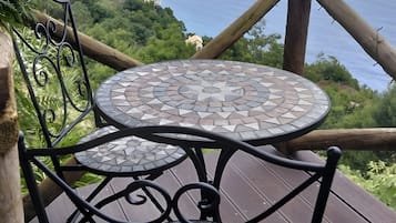 Een terras met een mozaiektafel en stoelen, met uitzicht op een kustlandschap met huizen.