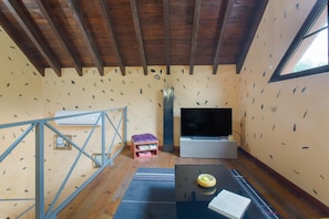 A room with a wooden ceiling, a large flat-screen TV, a small wooden table with a bowl, and a window.