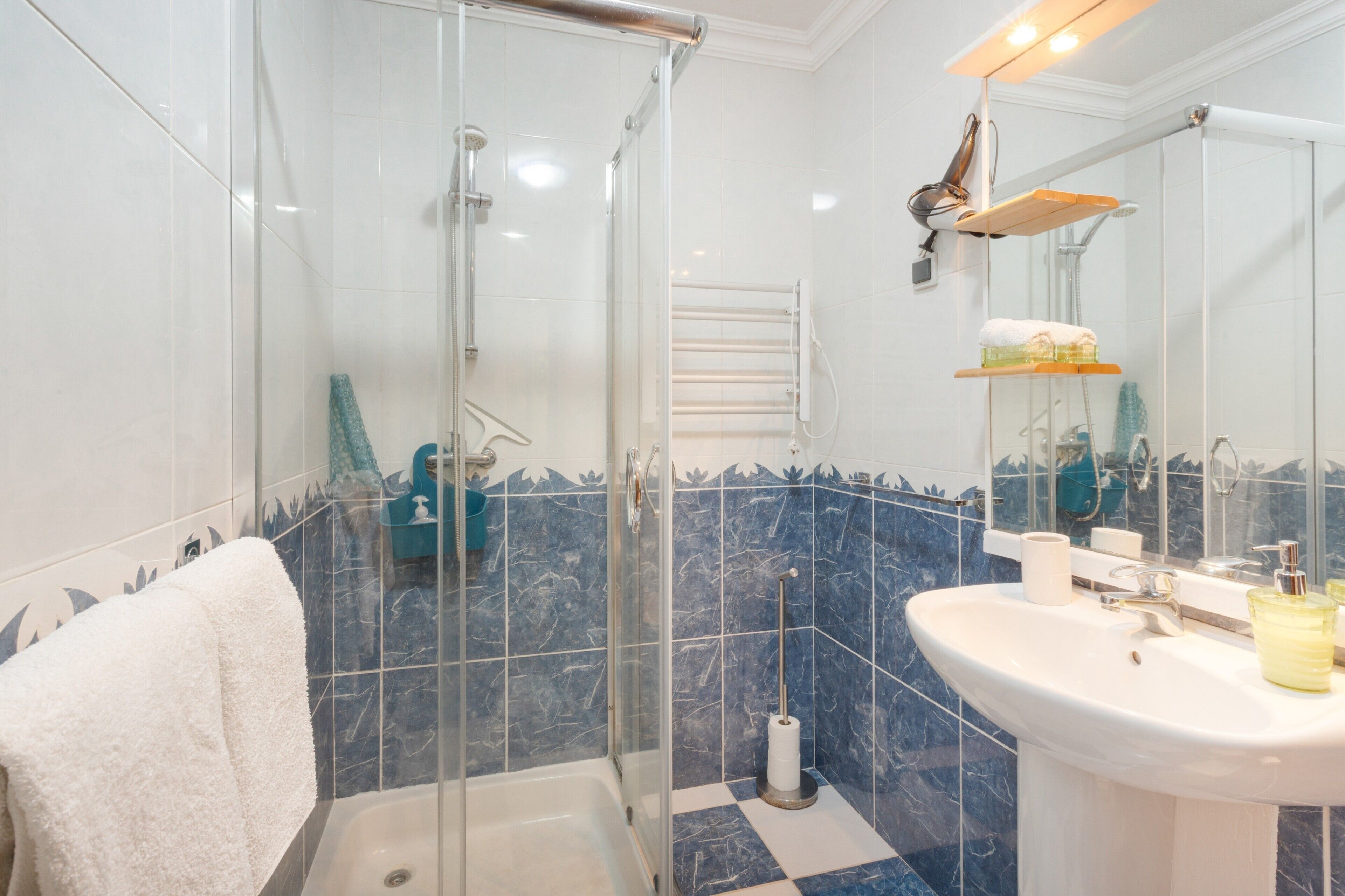 A bathroom with a glass shower enclosure, a white sink with a mirror, and a blue-tiled wall.