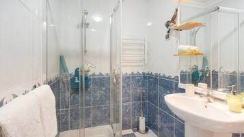 A bathroom with a glass shower enclosure, a white sink with a mirror, and a blue-tiled wall.