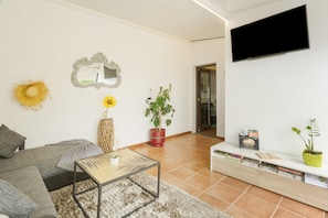 A living room with a sofa, a coffee table, a TV, a bookshelf, and a potted plant.