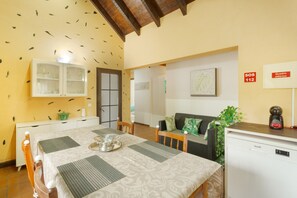 A dining area with a table set for four, a cabinet with glass doors, a sofa, a small refrigerator, and a wall-mounted sign.