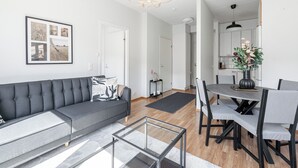 A modern living room with a gray sofa, a glass coffee table, and a dining area with a table and chairs. - Comfy 1BR Apt with Sauna - Best Location (Jyväskylä)