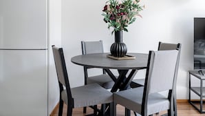 A dining area with a round table, four chairs, a vase with flowers, a refrigerator, and a lamp. - Comfy 1BR Apt with Sauna - Best Location (Jyväskylä)