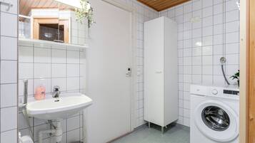 A compact bathroom with a sink, toilet paper, a washing machine, and a mirror.