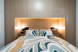 Ein Bett mit einem gemusterten Überwurf, zwei Nachttischlampen und einem hölzernen Kopfteil.