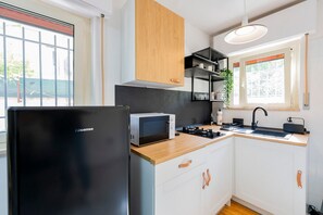 Eine kleine Küche mit einem schwarzen Kühlschrank, einer Mikrowelle, einer Holzausziehtafel und einem schwarzen Spülbecken.