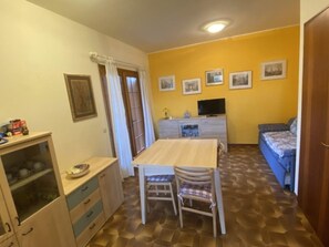 Ein gemütlicher Raum mit Esstisch, Stühlen, einer Couch, einem Fernseher und einem Schrank.