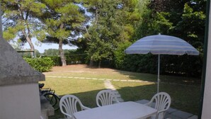 Un patio al aire libre con una mesa y sillas, un paraguas a rayas y vistas a un césped con árboles.