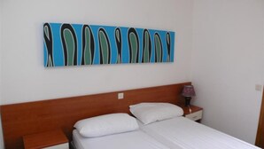 Una habitación con una cama, una mesita de noche, una lámpara y una obra de arte en la pared.