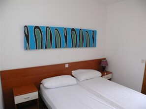 Ein Zimmer mit Bett, Nachttisch, Lampe und einem Wandbild.